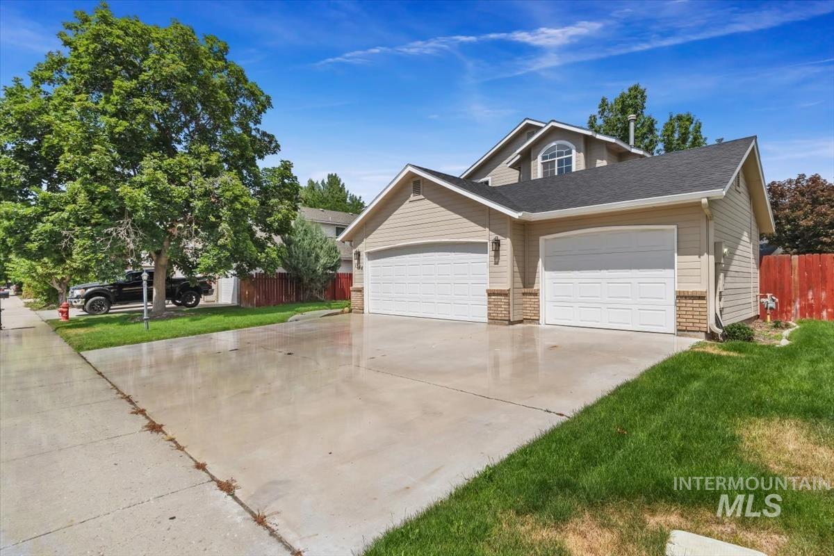 Front exterior featuring light tan siding, a two-car garage with white panel doors, and brick accents