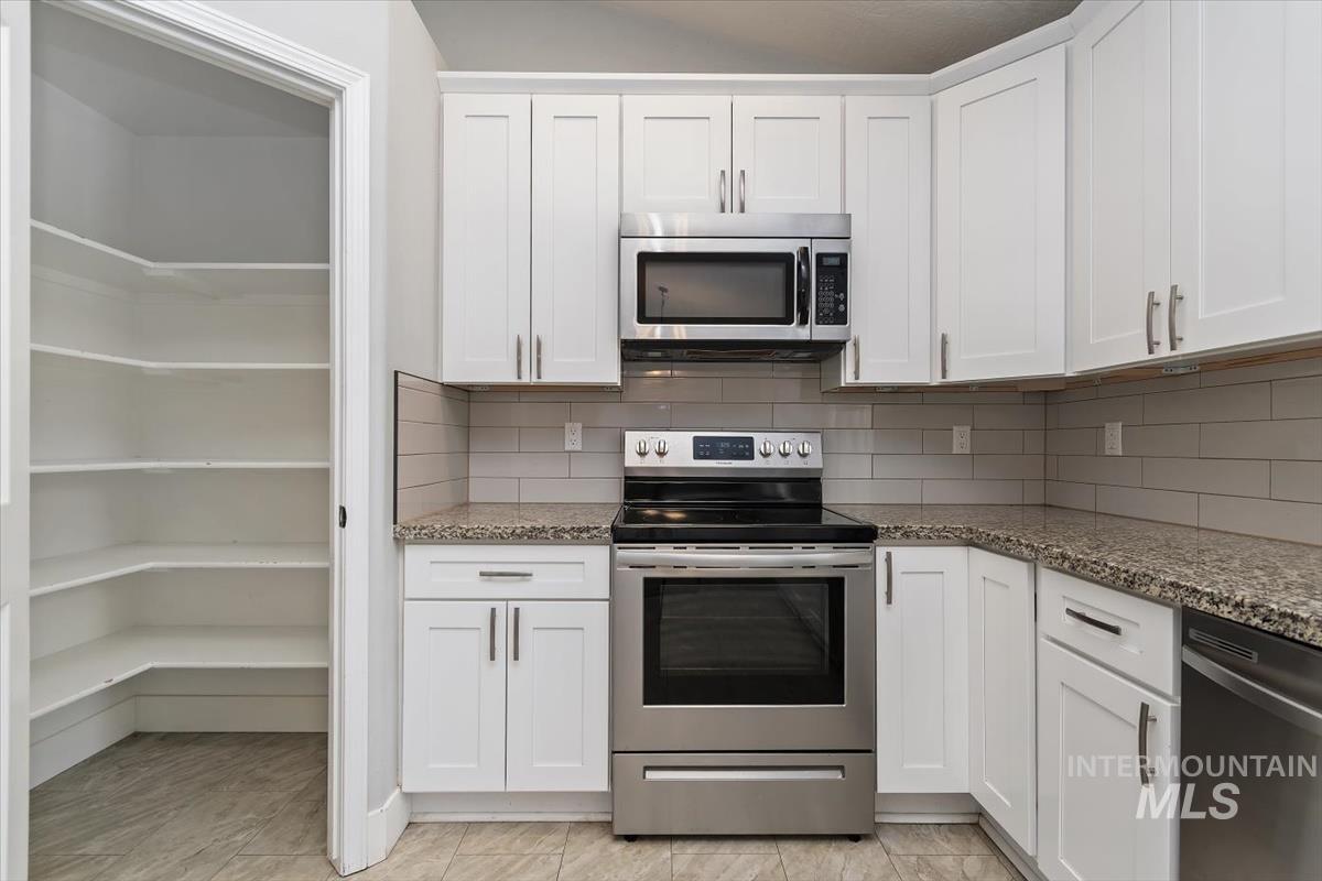 Kitchen featuring white cabinetry, stone-finish countertops, subway tile backsplash, and stainless steel appliances including a built-in microwave, range, and dishwasher
