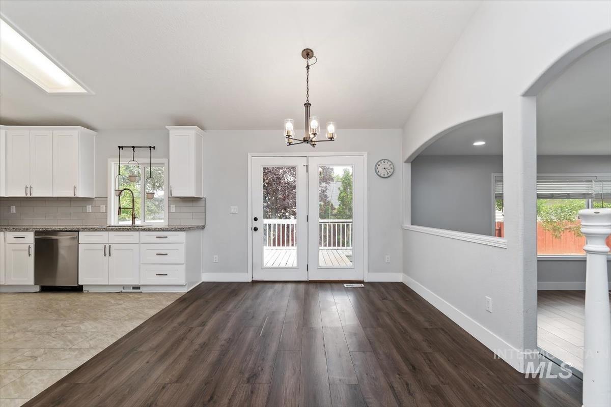 Open-concept common area featuring wood-finish flooring, white cabinetry, stainless steel dishwasher, and patio door access