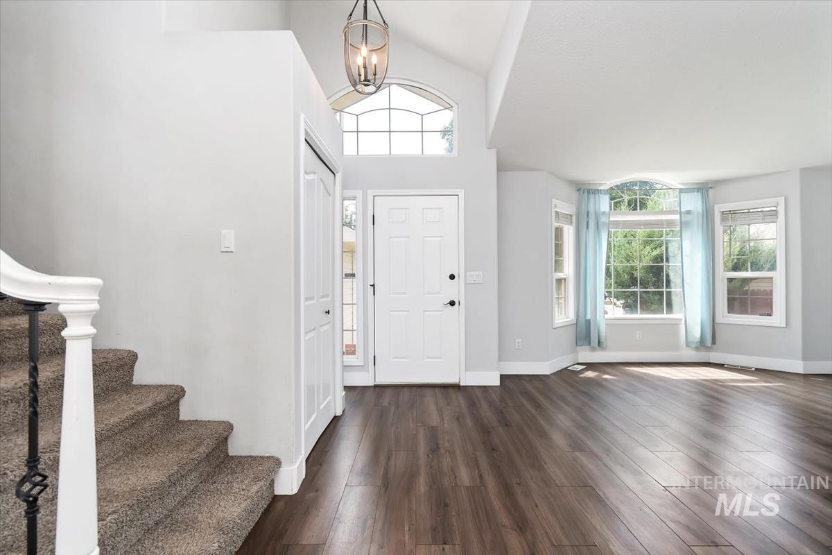 Entryway featuring vaulted ceilings, wood-finish flooring, a contemporary chandelier, and a prominent bay window
