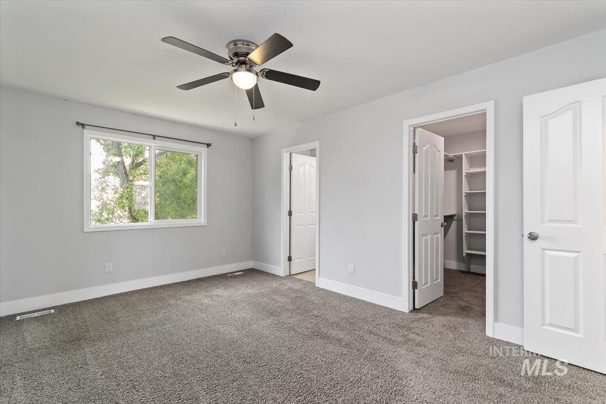 Carpeted bedroom featuring a ceiling fan with integrated lighting, a large window with white trim, and a walk-in closet with built-in shelving