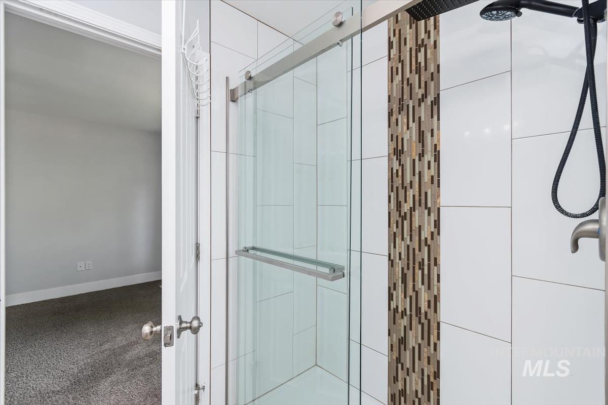Shower enclosure featuring a glass sliding door, white rectangular wall tiles, a vertical mosaic tile accent, and a matte black shower head and handheld sprayer