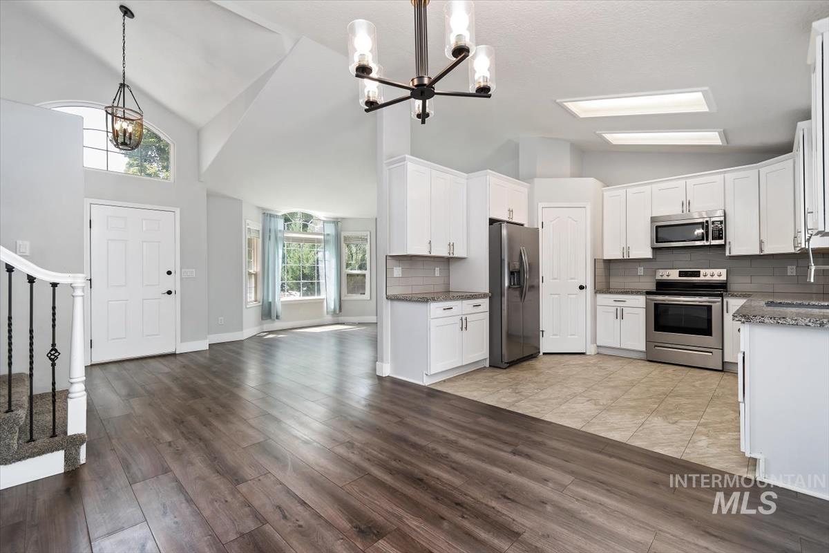 Open-concept interior featuring wood-finish flooring, vaulted ceilings, a kitchen with white cabinetry and stainless steel appliances, and a bay window in the living area