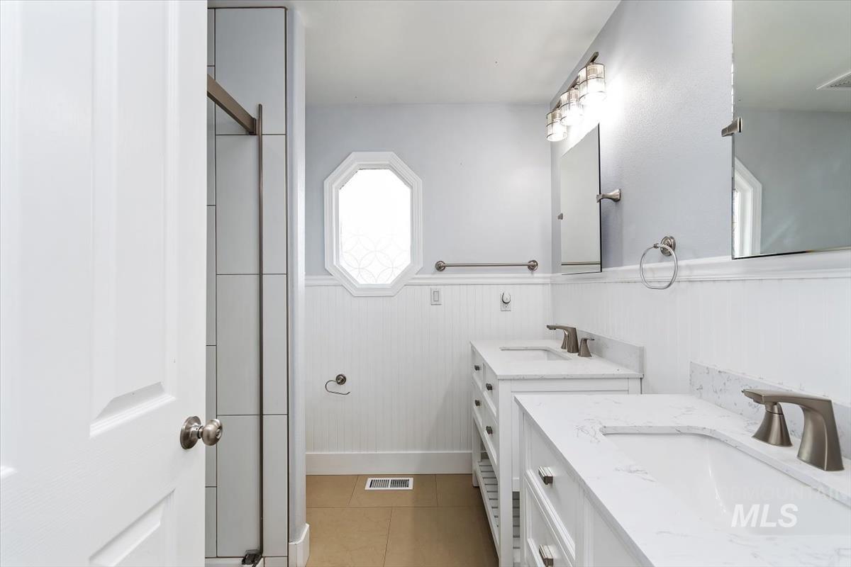 Bathroom with dual vanity sinks, white cabinetry, and a tile shower with clear glass enclosure
