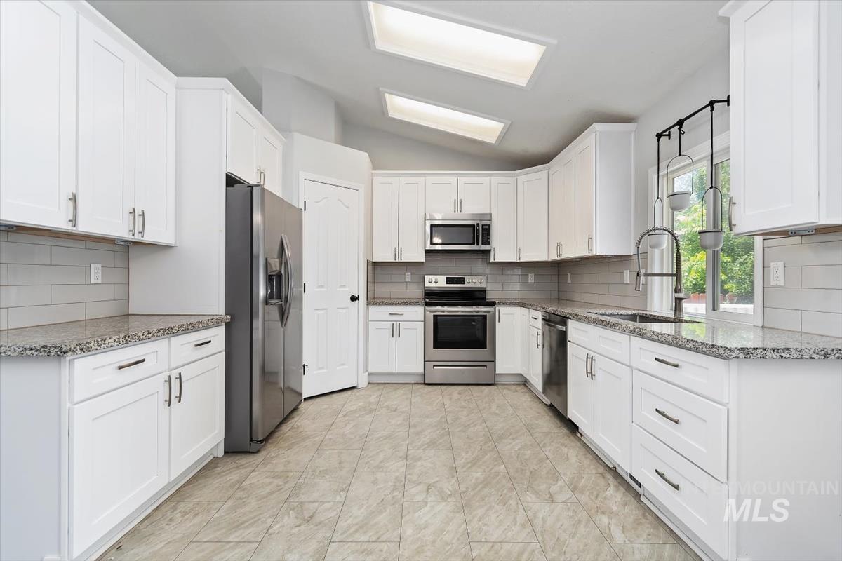 Spacious kitchen featuring extensive white cabinetry, granite countertops, stainless steel appliances, a subway tile backsplash, and two skylights