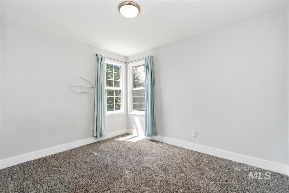 Bright interior space featuring a corner window configuration with grid panes, plush carpeting, and crisp white baseboards