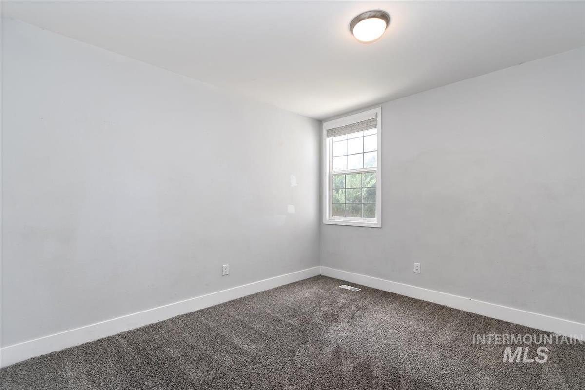 Bright room featuring a window with white trim, gray textured carpeting, and a flush mount ceiling light fixture
