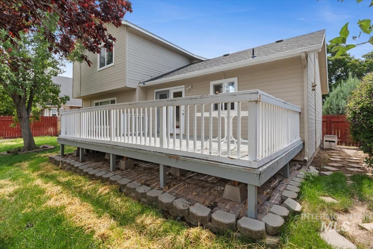 Rear exterior featuring a spacious elevated deck with white railing, tan siding, and a red privacy fence