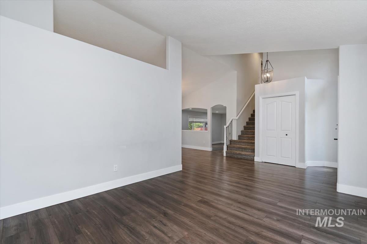 Open entryway featuring wood-finish flooring, a contemporary pendant light fixture, a staircase with a white railing, and a double-door closet