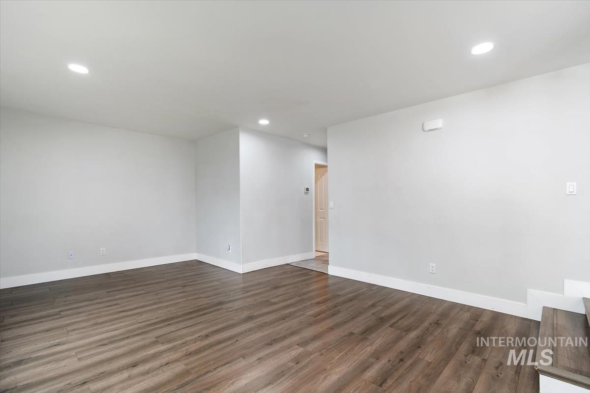 Spacious room featuring wood-finish flooring, recessed lighting, light gray walls, and white baseboards