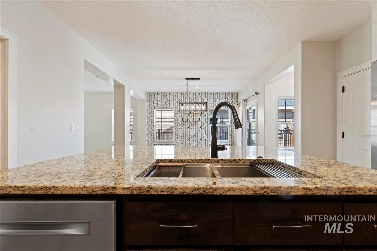 Kitchen with dark brown cabinetry, a chandelier, light stone countertops, dishwasher, and a textured ceiling