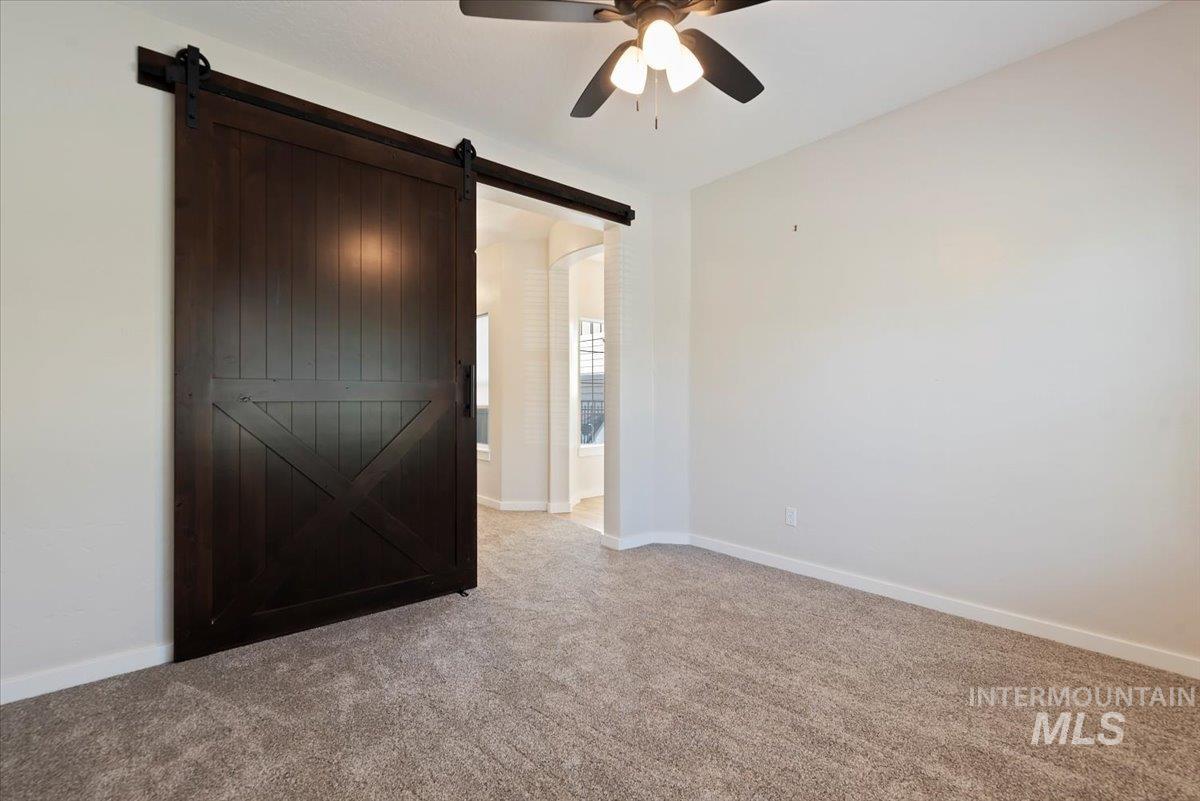 Unfurnished bedroom with light carpet, a barn door, a ceiling fan, and ensuite bathroom
