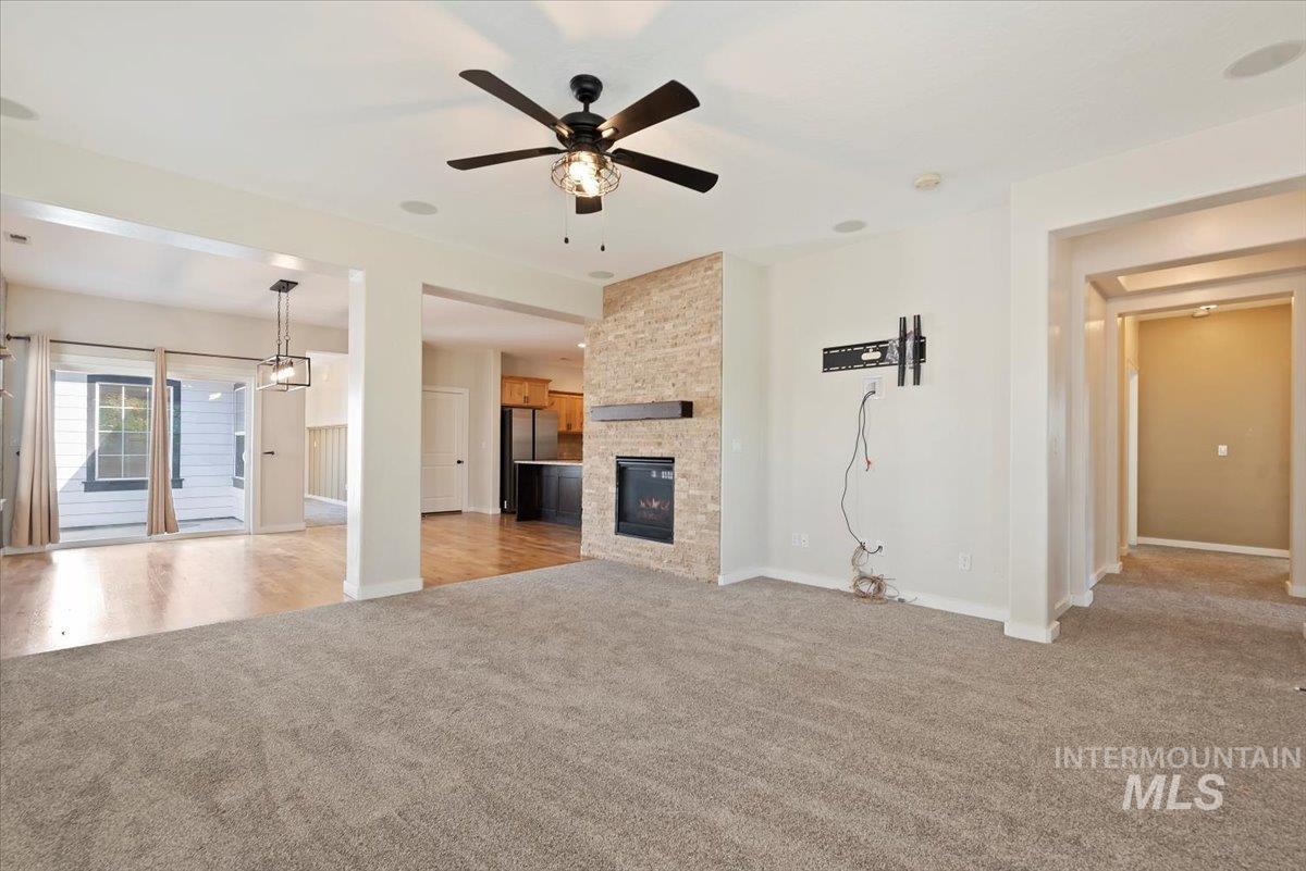 Unfurnished living room with light colored carpet, a large fireplace, and a ceiling fan