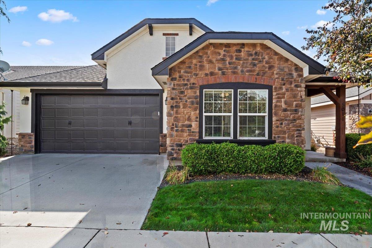 View of front of home with stone siding, driveway, a garage, and roof with shingles