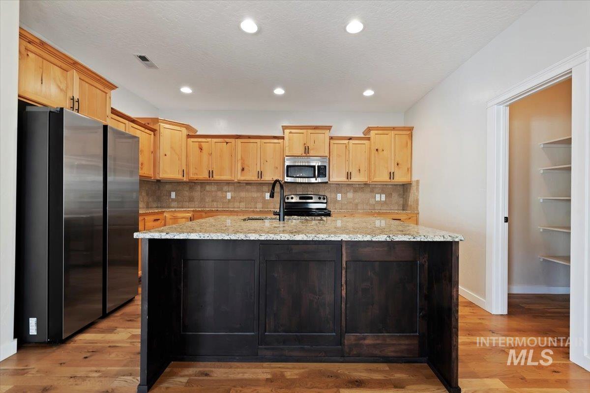 Kitchen featuring decorative backsplash, light brown cabinetry, stainless steel appliances, light stone countertops, and recessed lighting