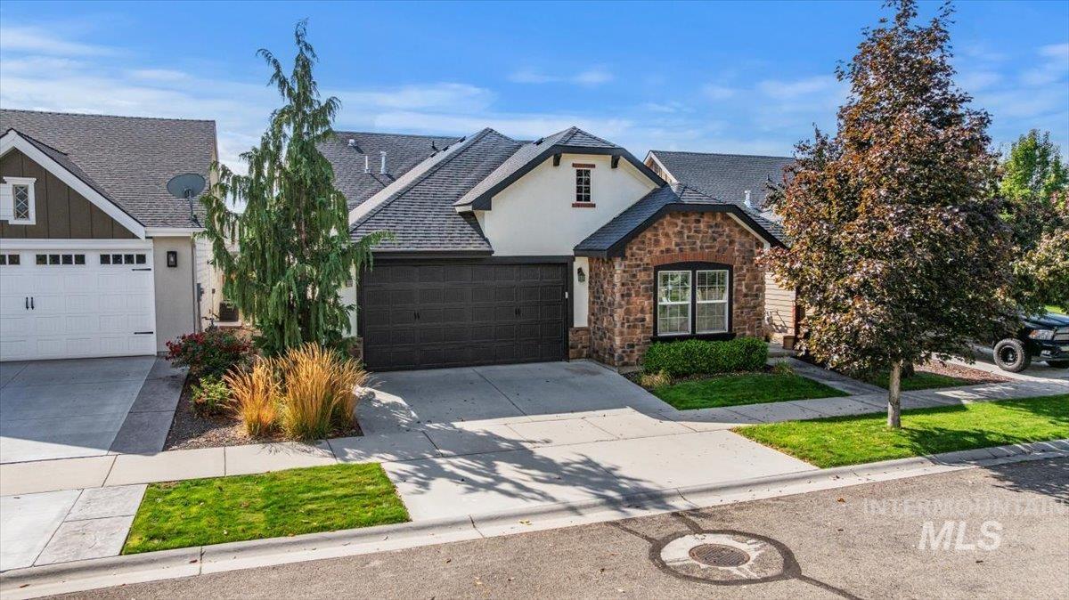 View of front of home featuring stucco siding, driveway, roof with shingles, stone siding, and an attached garage