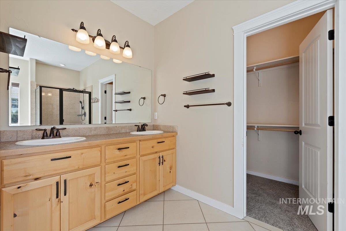 Full bath with a shower stall, a walk in closet, light tile patterned flooring, and double vanity