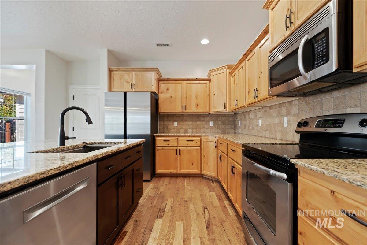 Kitchen with stainless steel appliances, light brown cabinetry, backsplash, and recessed lighting