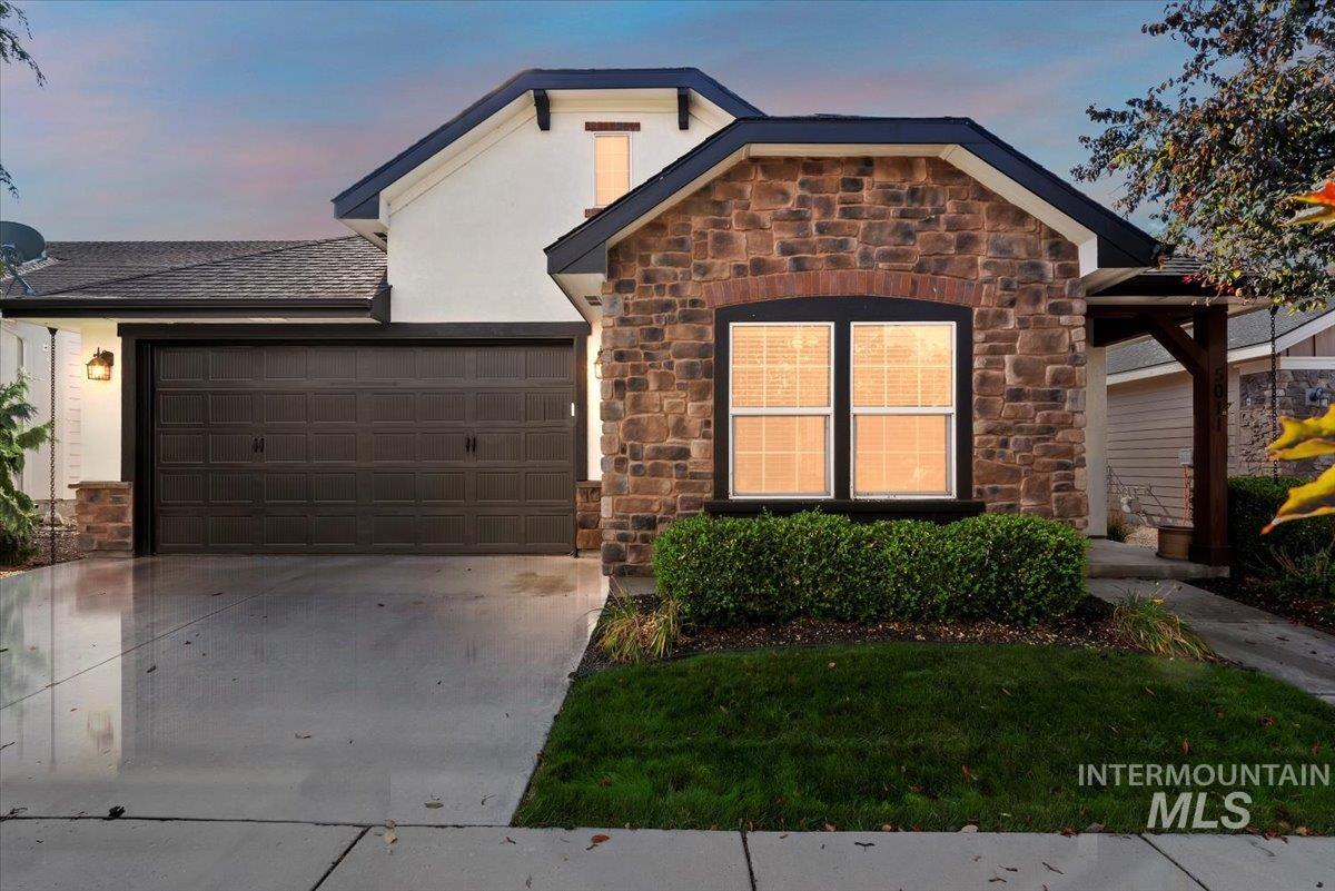 View of front facade with stone siding, concrete driveway, a garage, and stucco siding