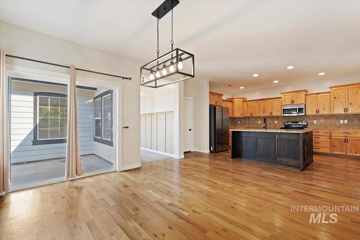 Kitchen with decorative light fixtures, appliances with stainless steel finishes, light wood-style flooring, a kitchen island with sink, and tasteful backsplash