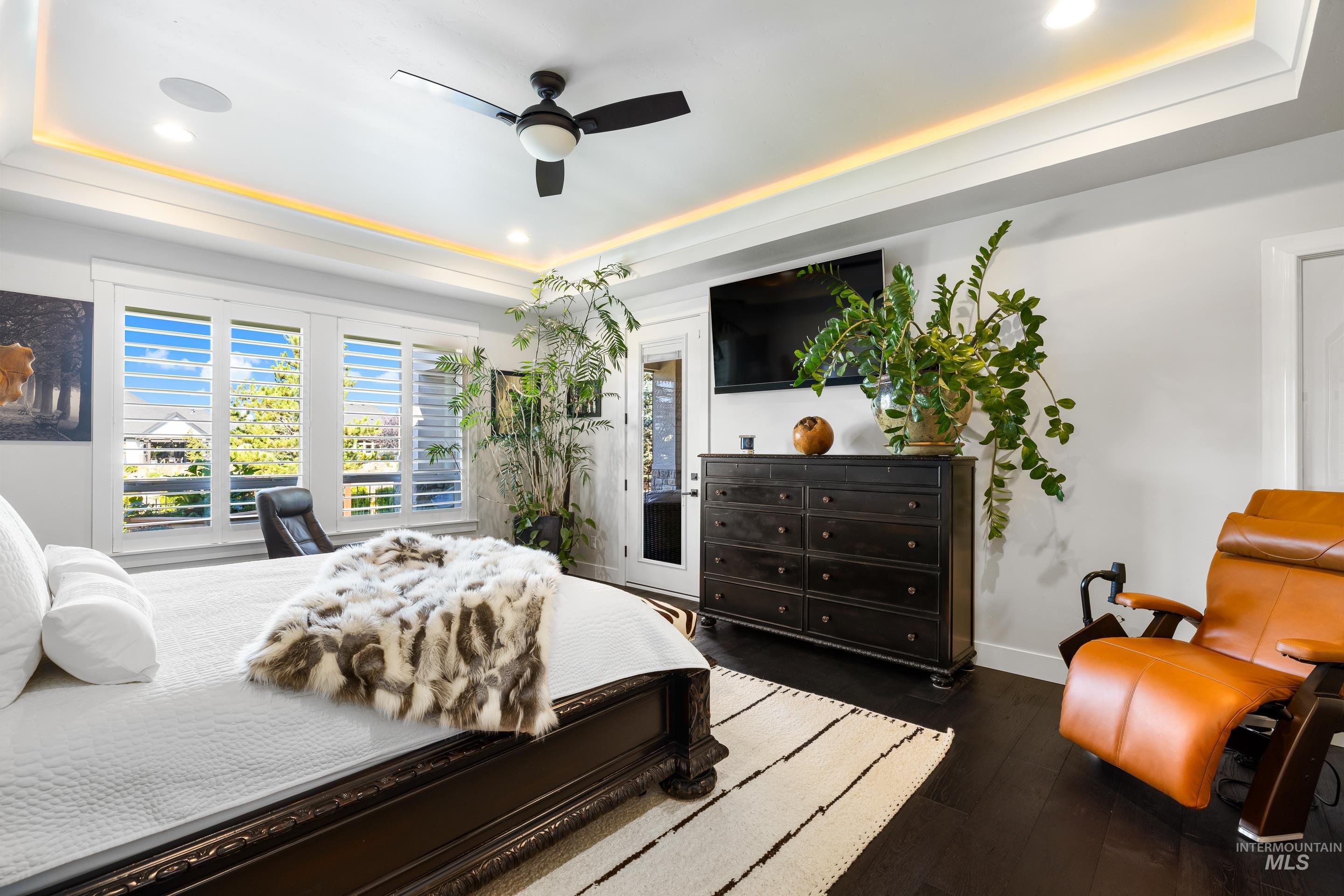 Bedroom with a raised ceiling, dark wood finished floors, recessed lighting, and ceiling fan