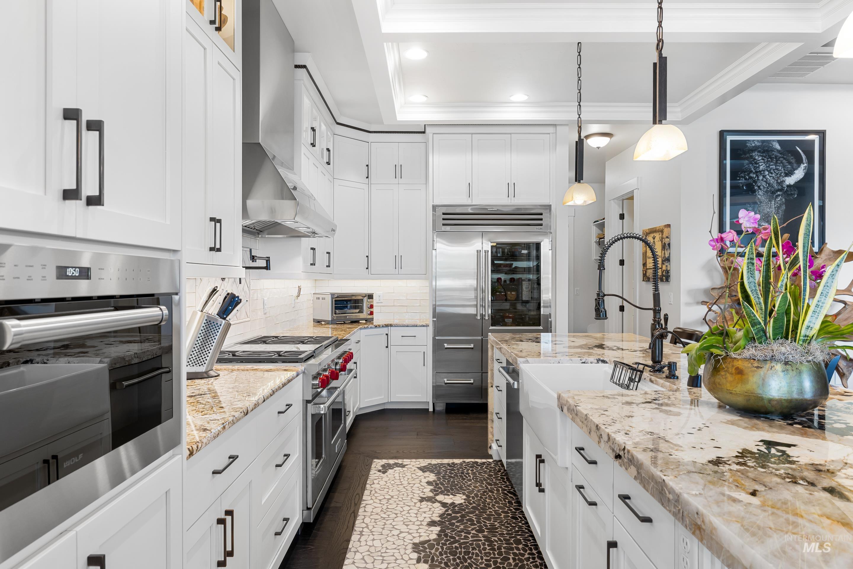 Kitchen featuring high quality appliances, hanging light fixtures, tasteful backsplash, white cabinets, and light stone counters