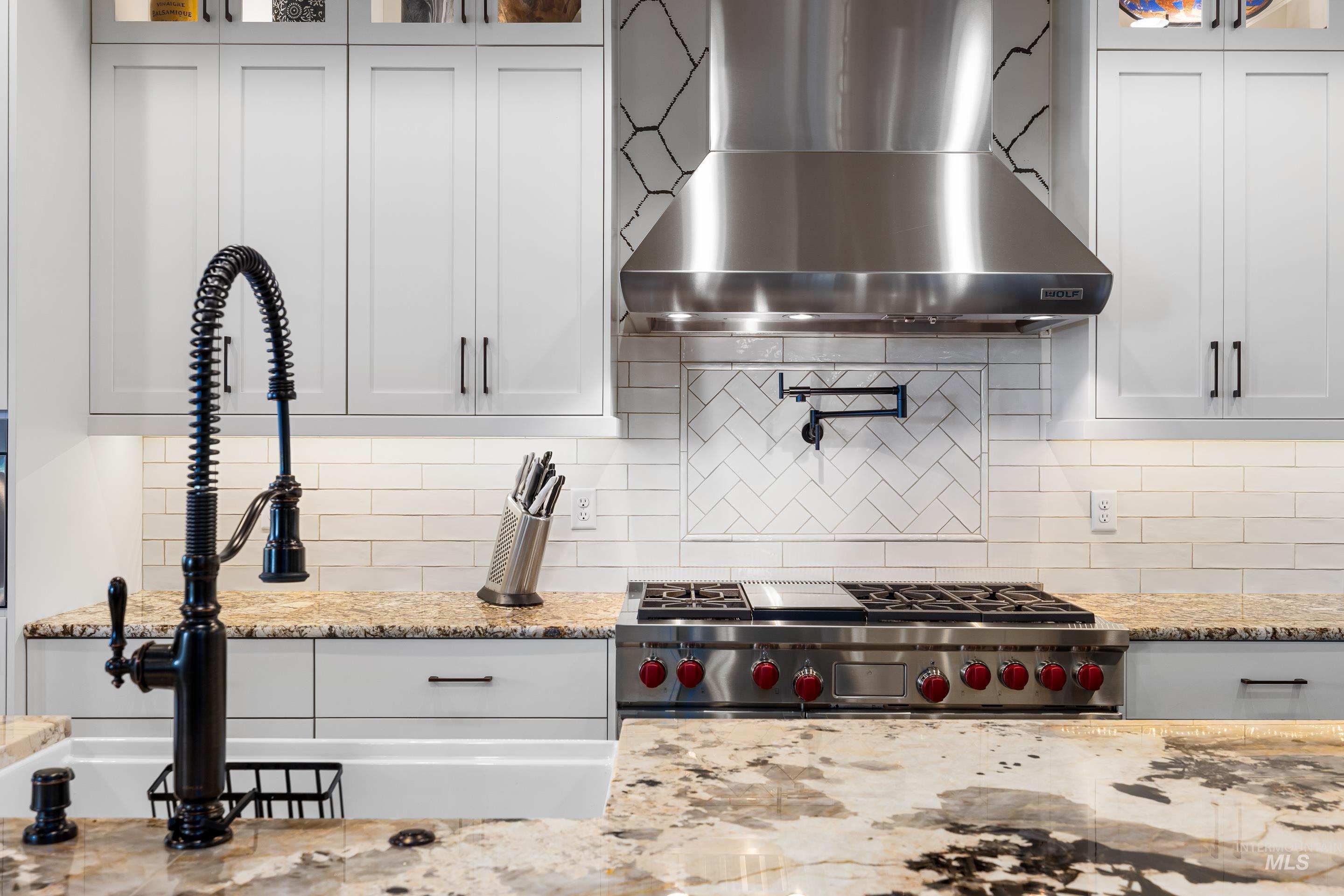 Kitchen featuring wall chimney exhaust hood, glass insert cabinets, white cabinets, light stone countertops, and decorative backsplash