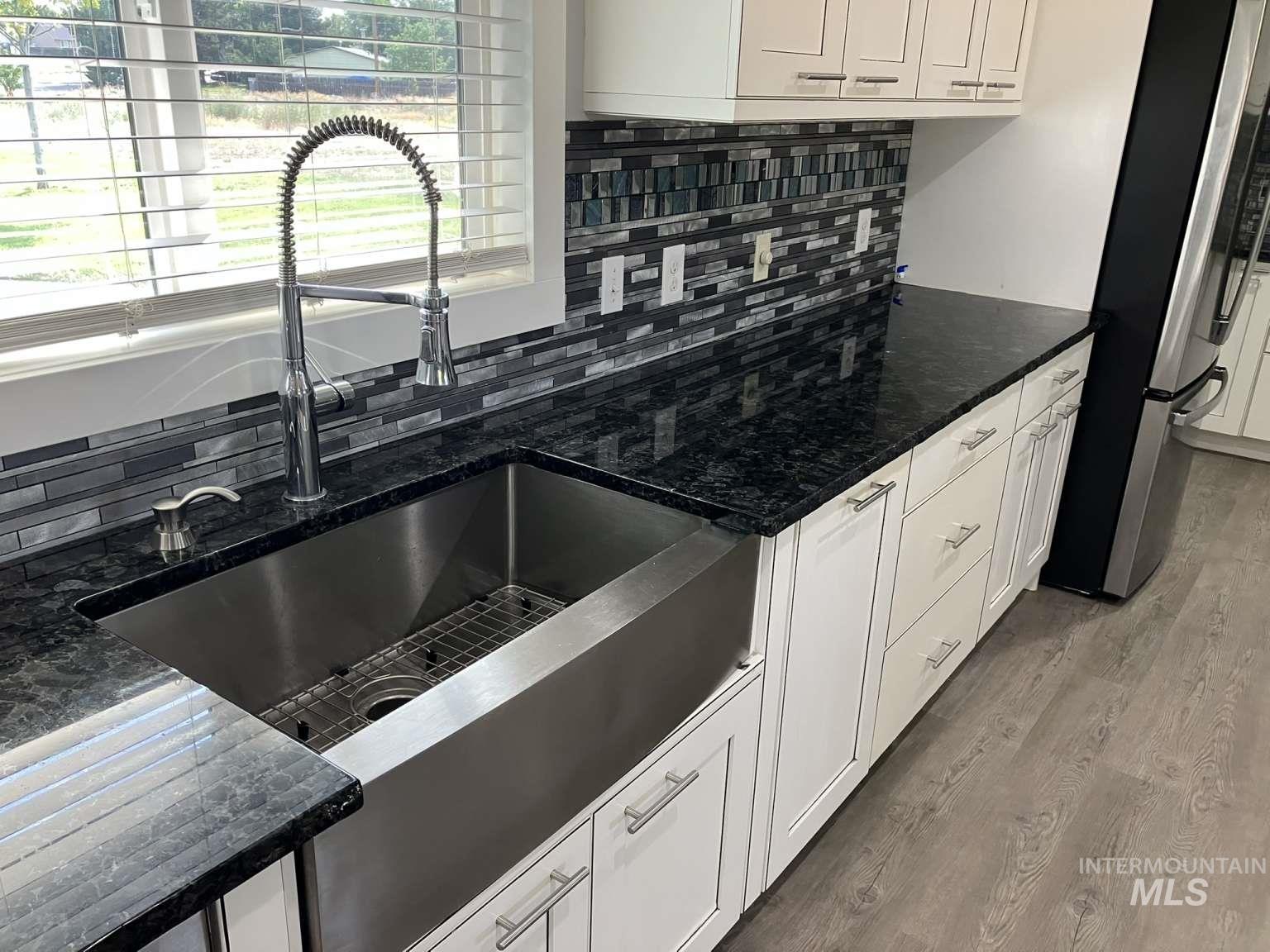 Kitchen featuring freestanding refrigerator, tasteful backsplash, white cabinets, light wood-type flooring, and dark stone counters
