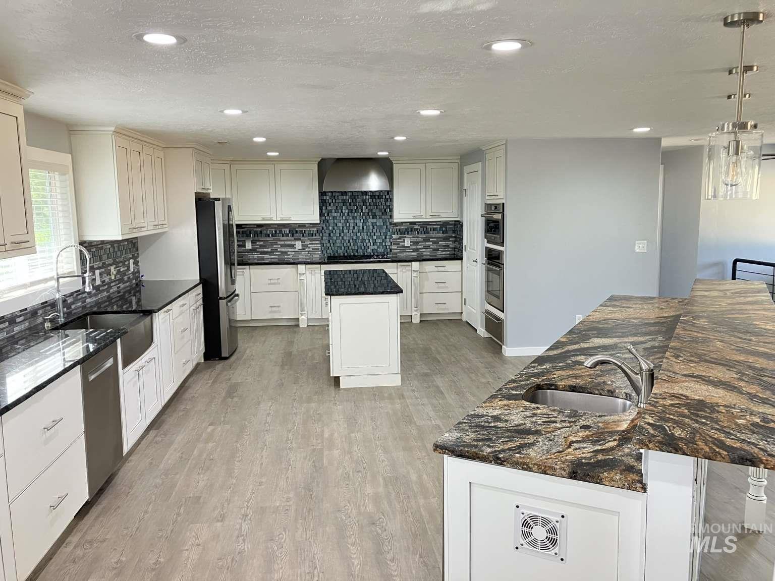 Kitchen with a kitchen island with sink, recessed lighting, decorative backsplash, light wood finished floors, and stainless steel appliances