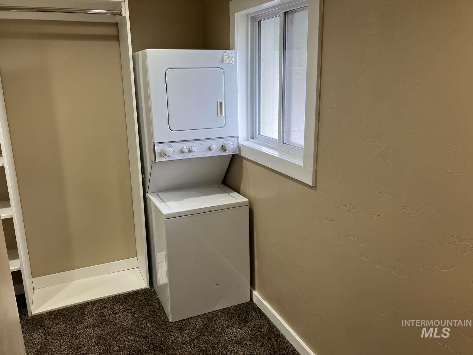 Washroom featuring stacked washer and clothes dryer and carpet floors