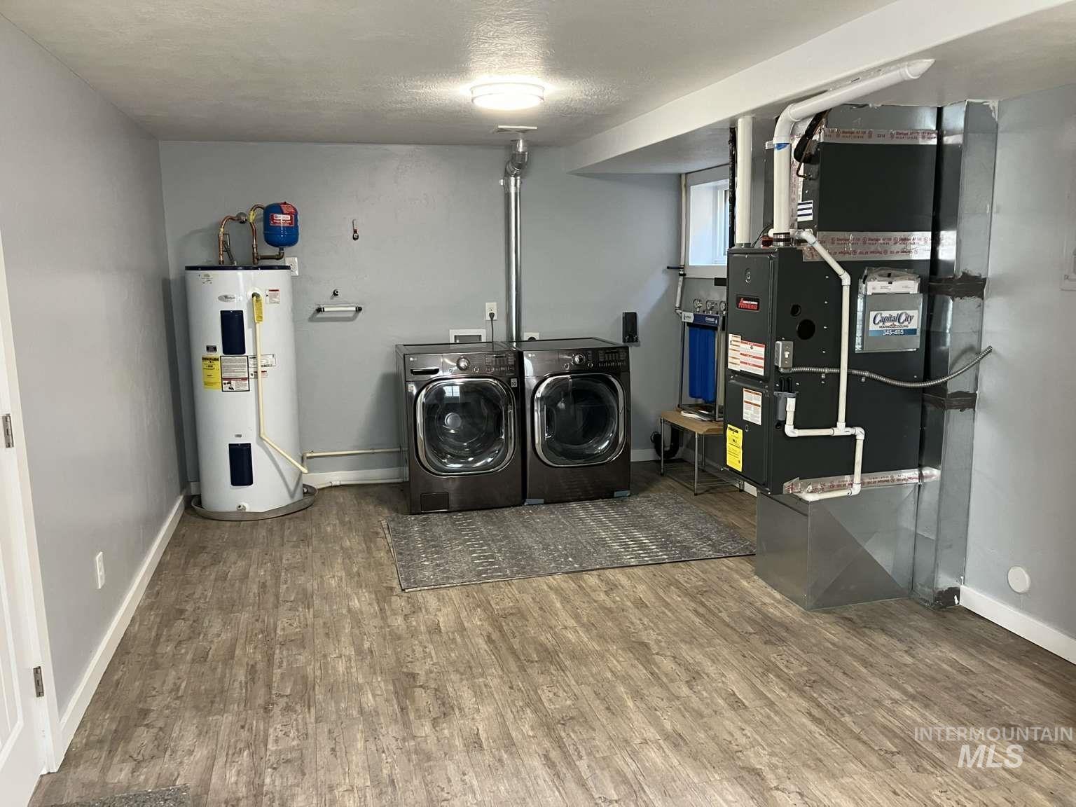 Laundry room with washer and clothes dryer, heating unit, electric water heater, wood finished floors, and a textured ceiling