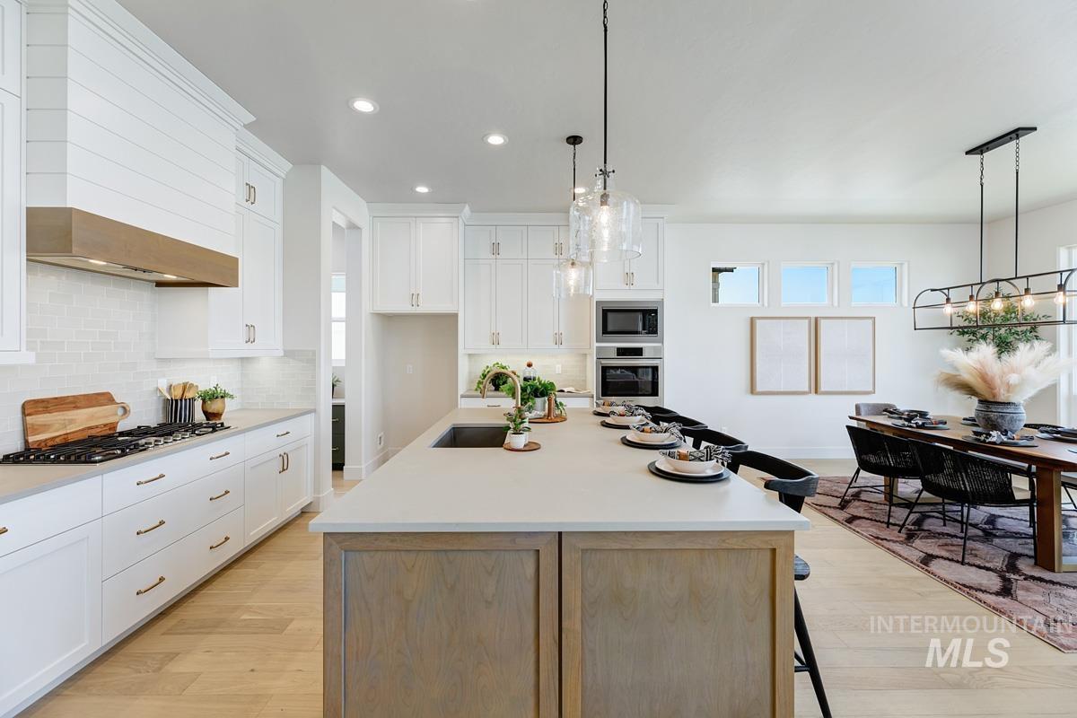 Dual tone kitchen featuring a breakfast bar, a center island with sink, light wood-type flooring, stainless steel appliances, and two tone color scheme