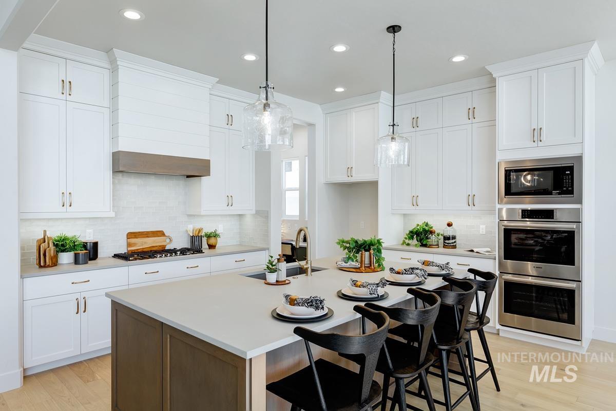 Dual tone kitchen with a breakfast bar area, an island with sink, stainless steel appliances, light wood-type flooring, and pendant lighting