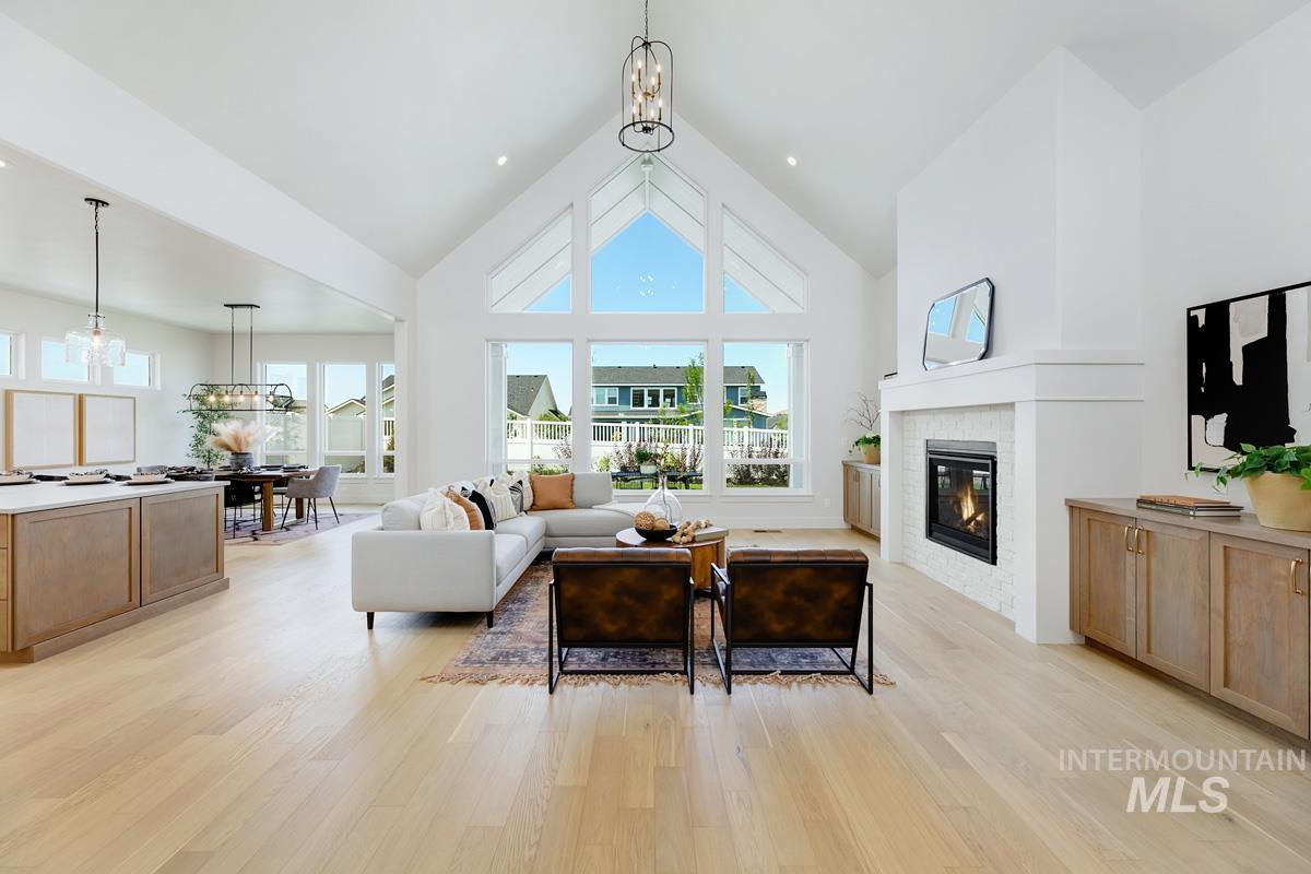 Living area featuring a chandelier, a high ceiling, a glass covered fireplace, and light wood-style flooring