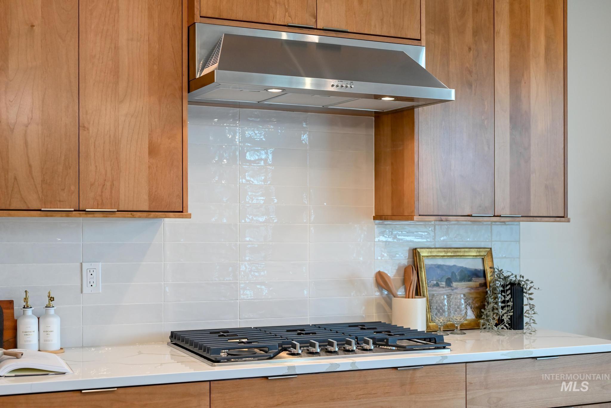 Kitchen with tasteful backsplash, under cabinet range hood, light stone counters, brown cabinets, and modern cabinets