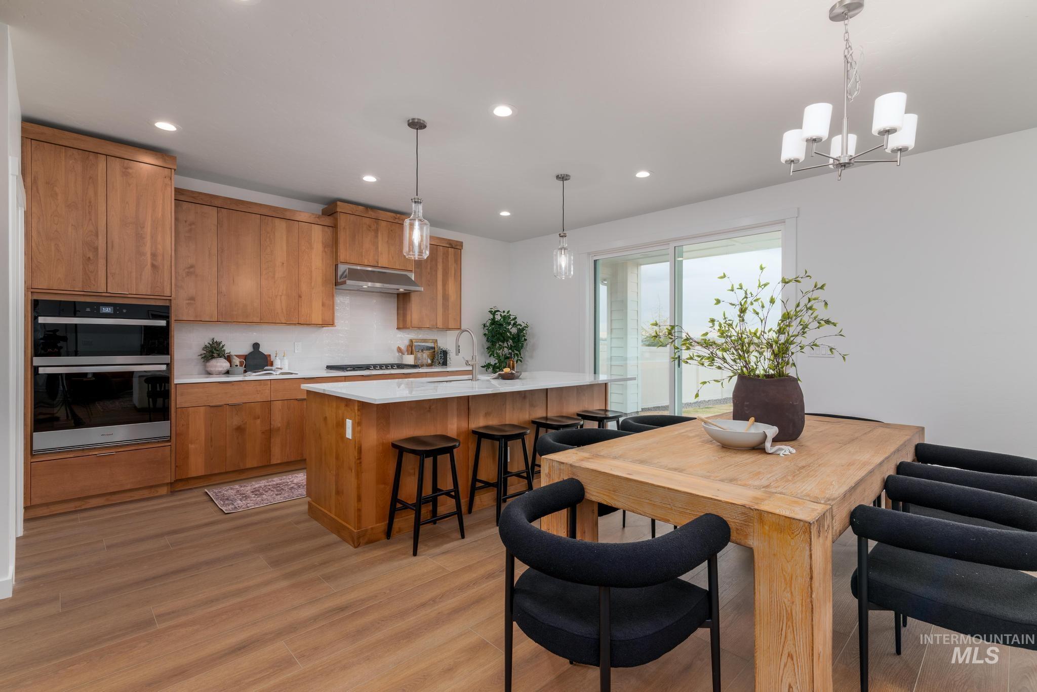 Kitchen with brown cabinetry, pendant lighting, decorative backsplash, a center island with sink, and recessed lighting