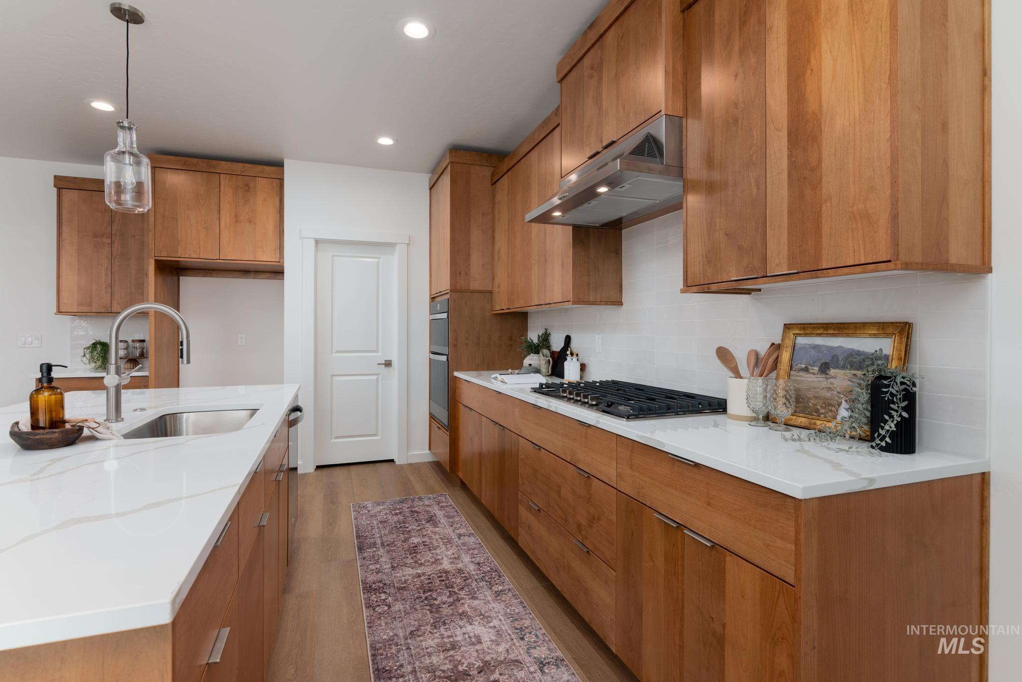 Kitchen with brown cabinets, decorative light fixtures, light wood-type flooring, light stone counters, and recessed lighting