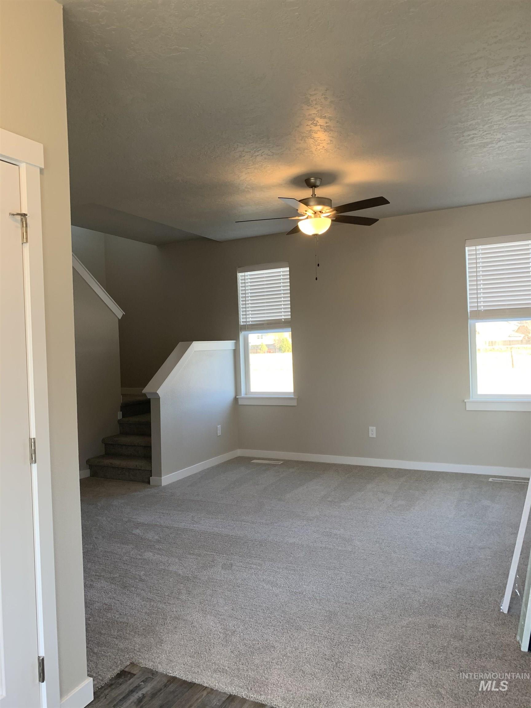 Unfurnished living room featuring carpet floors, a textured ceiling, and a ceiling fan