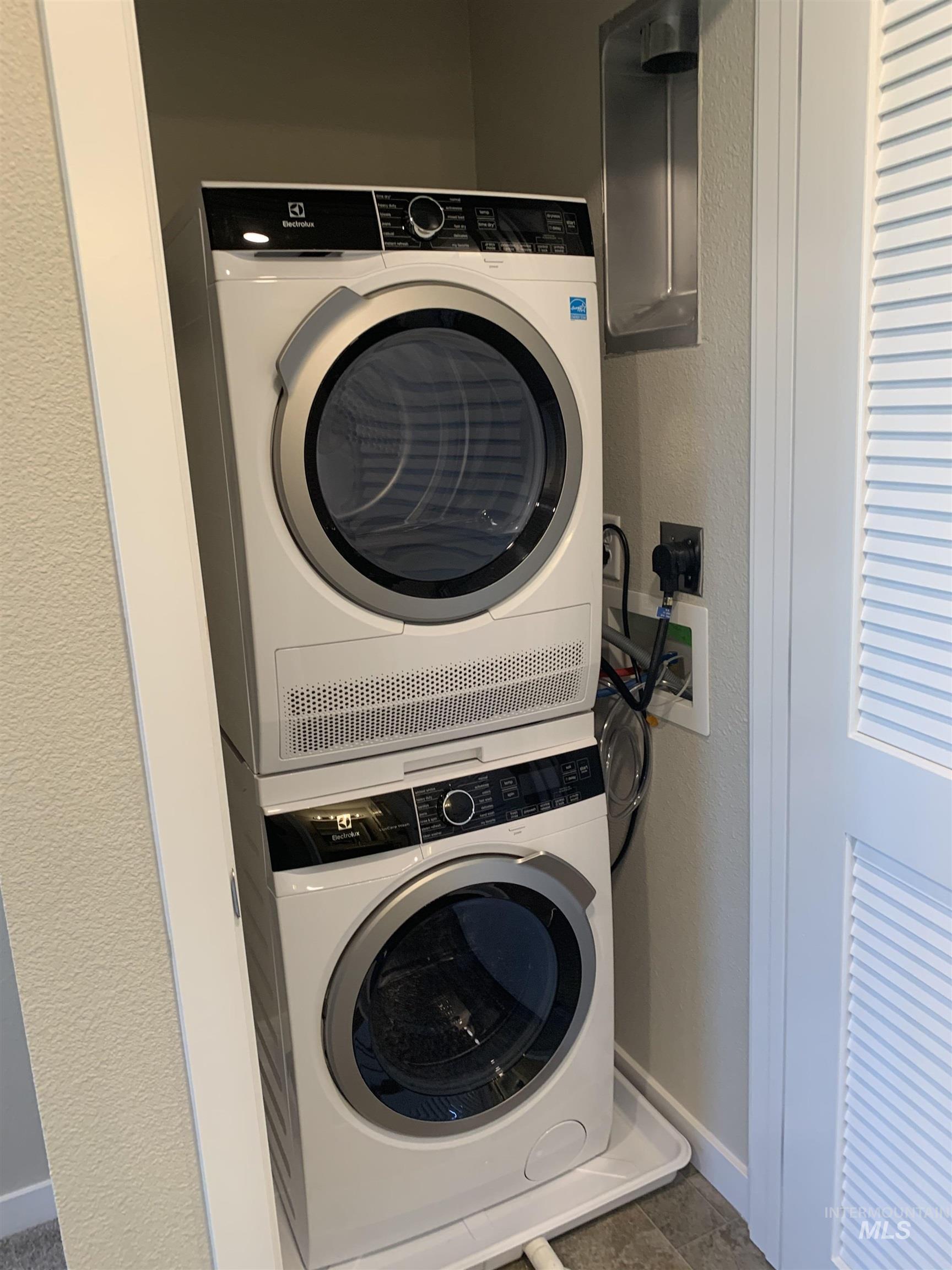 Laundry room featuring a textured wall and stacked washer and clothes dryer