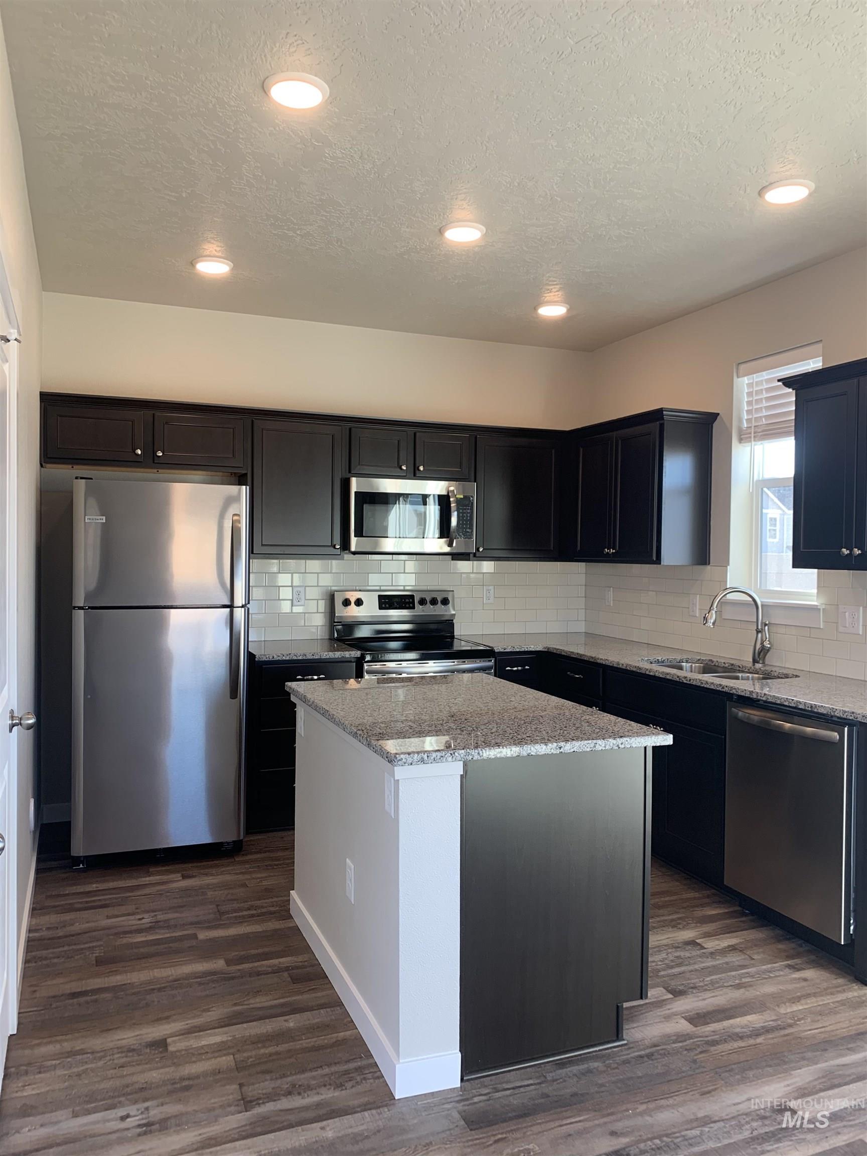 Kitchen featuring light stone counters, stainless steel appliances, a kitchen island, dark wood-type flooring, and backsplash