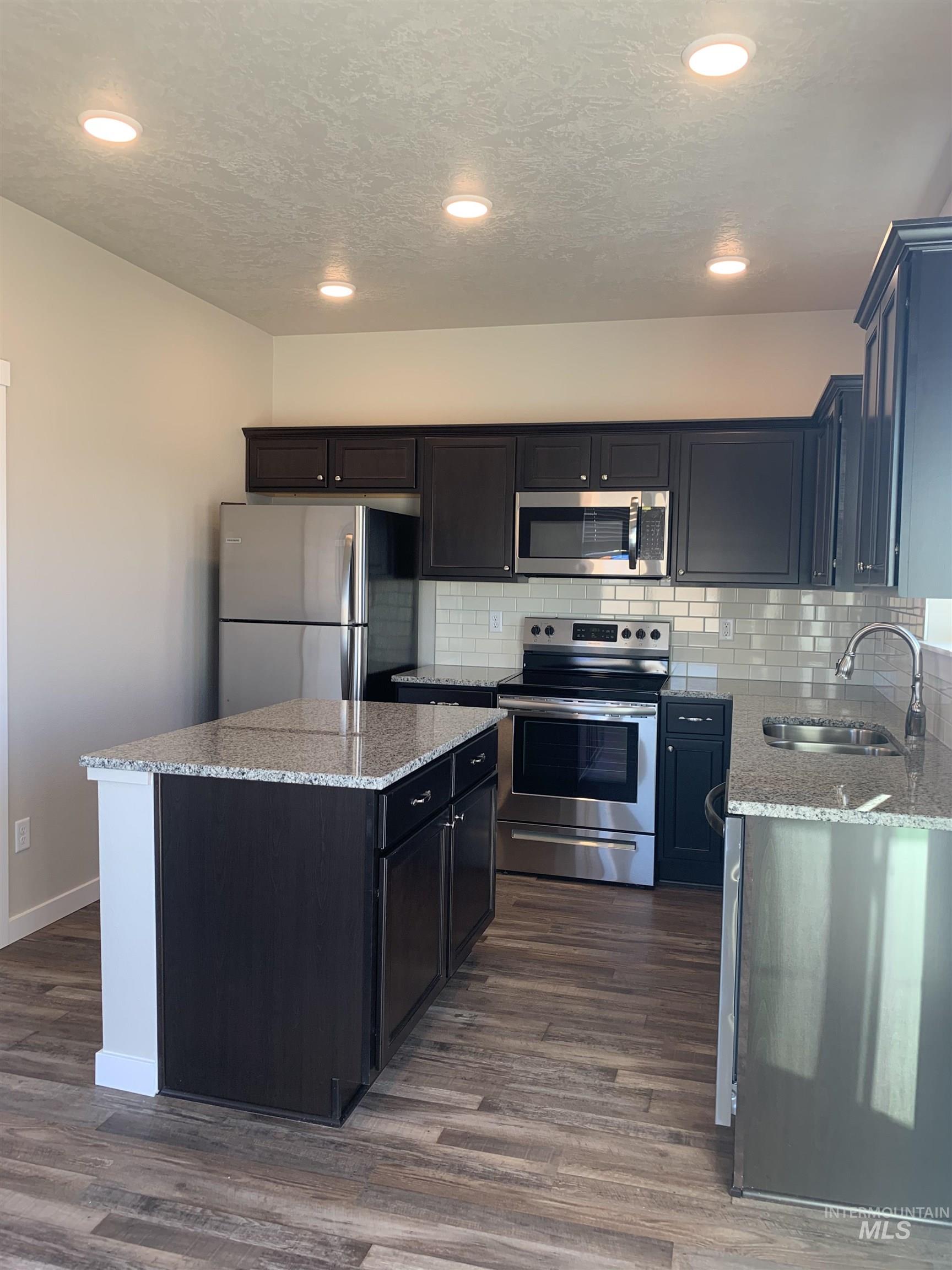 Kitchen featuring stainless steel appliances, light stone counters, a center island, tasteful backsplash, and dark wood finished floors