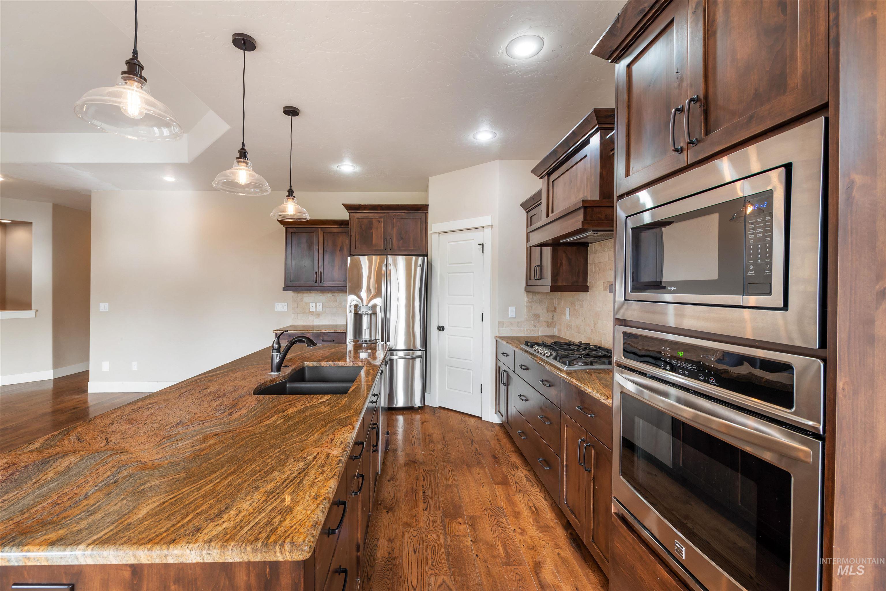 Kitchen featuring appliances with stainless steel finishes, hanging light fixtures, backsplash, dark brown cabinetry, and dark wood-style flooring