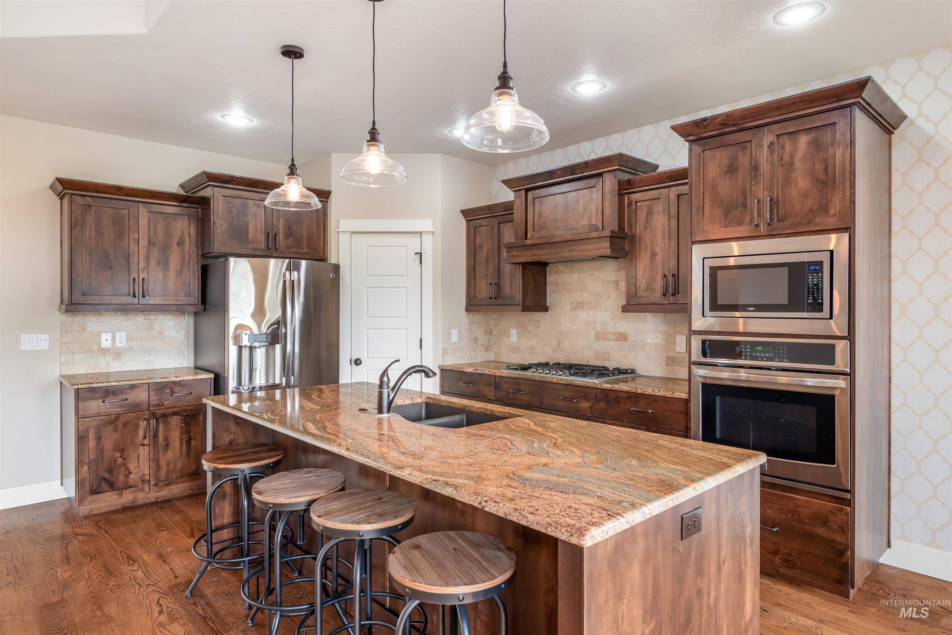 Kitchen with stainless steel appliances, light stone countertops, decorative backsplash, decorative light fixtures, and dark wood-style flooring