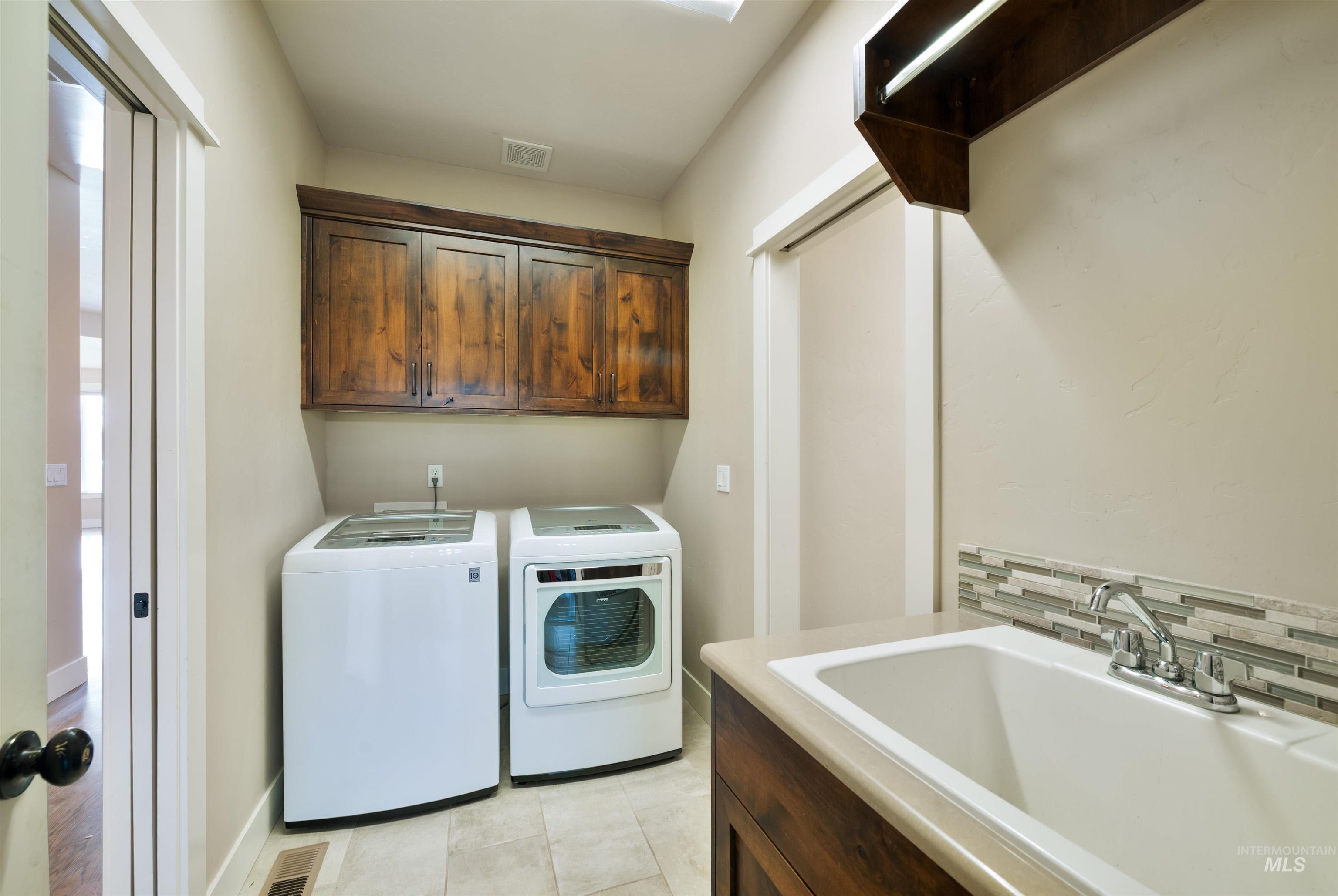 Washroom featuring washing machine and clothes dryer, cabinet space, and light tile patterned floors