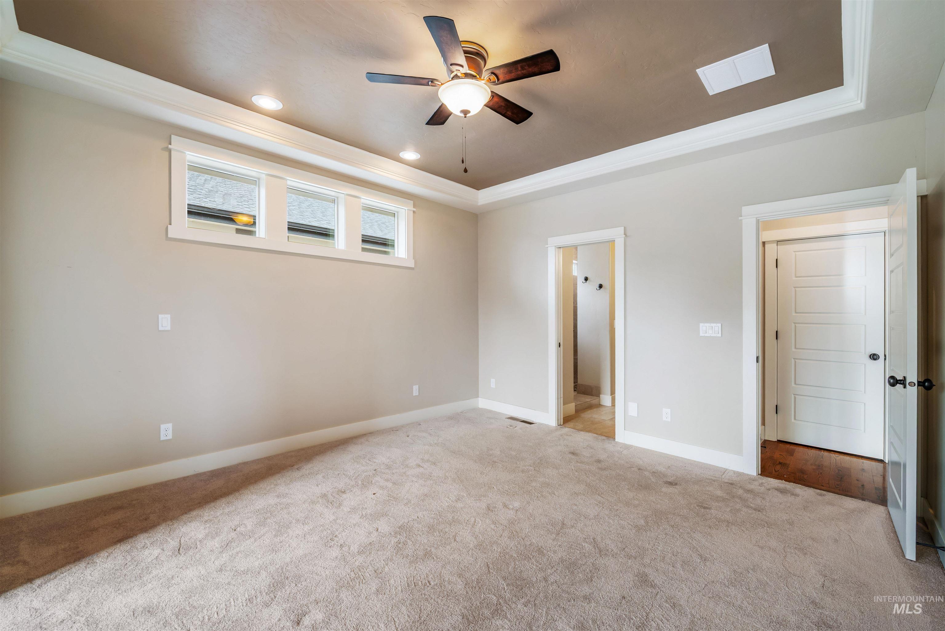 Unfurnished bedroom with a raised ceiling, ensuite bath, crown molding, recessed lighting, and carpet floors