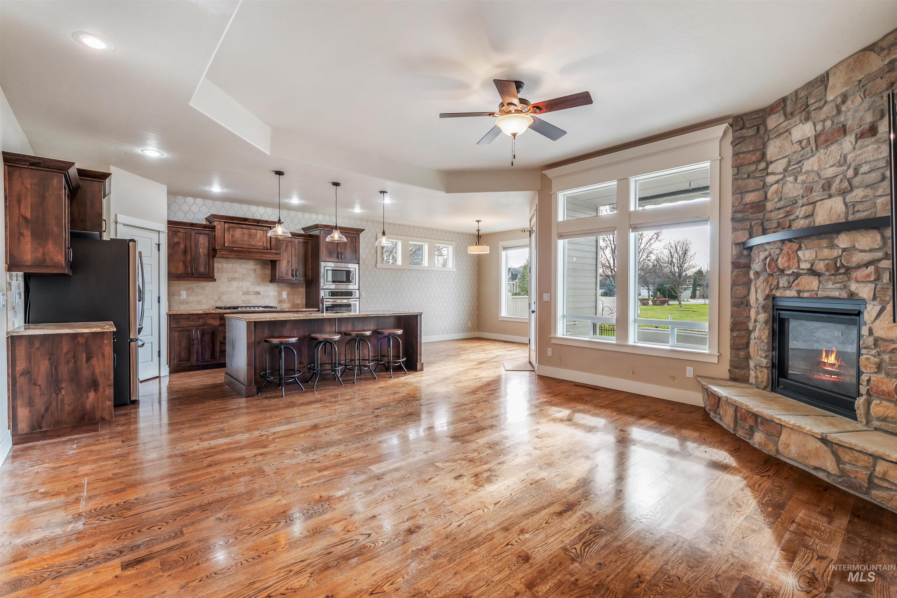 Unfurnished living room featuring a stone fireplace, ceiling fan, light wood-style floors, and a raised ceiling
