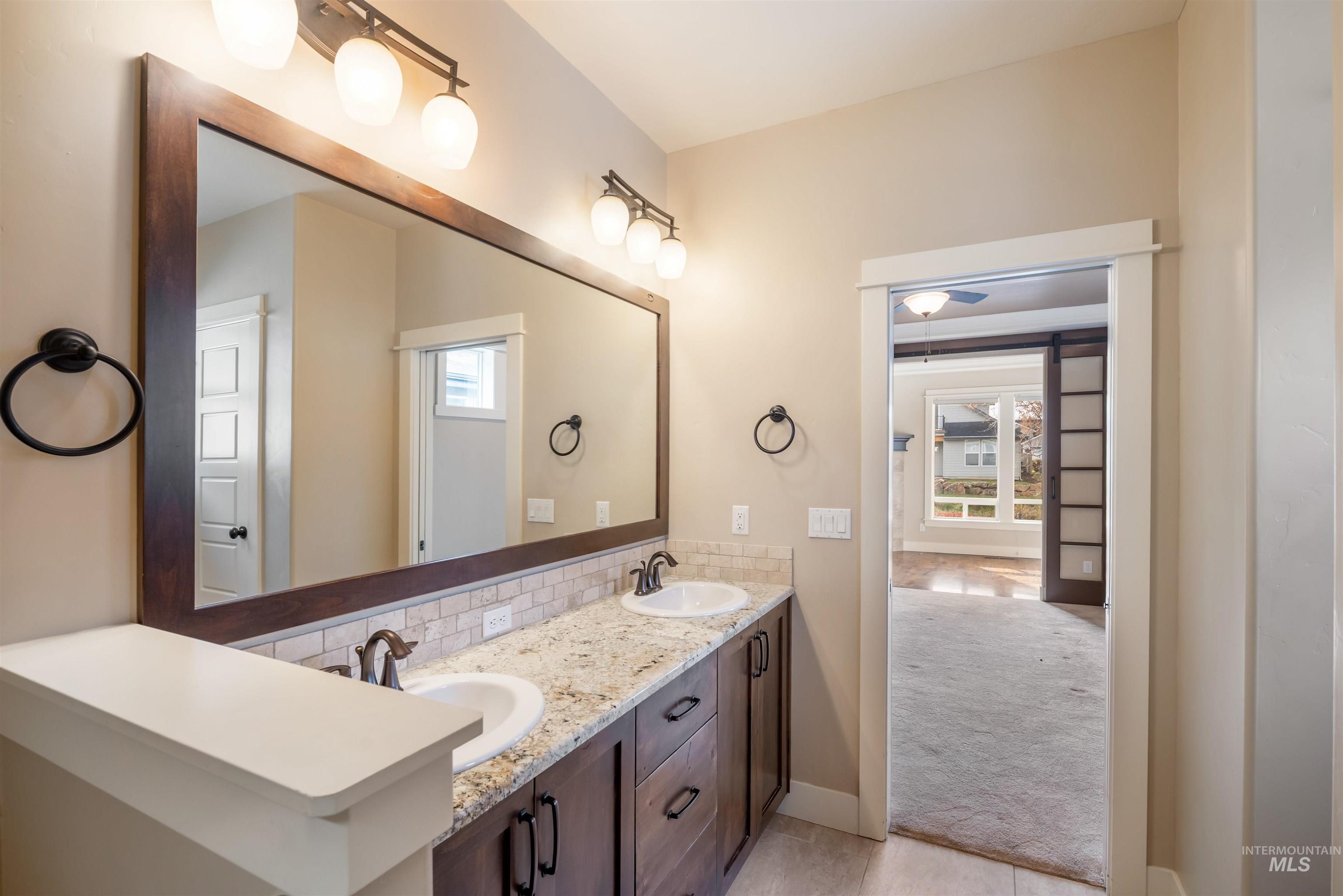 Full bath with double vanity, light carpet, backsplash, and light tile patterned flooring