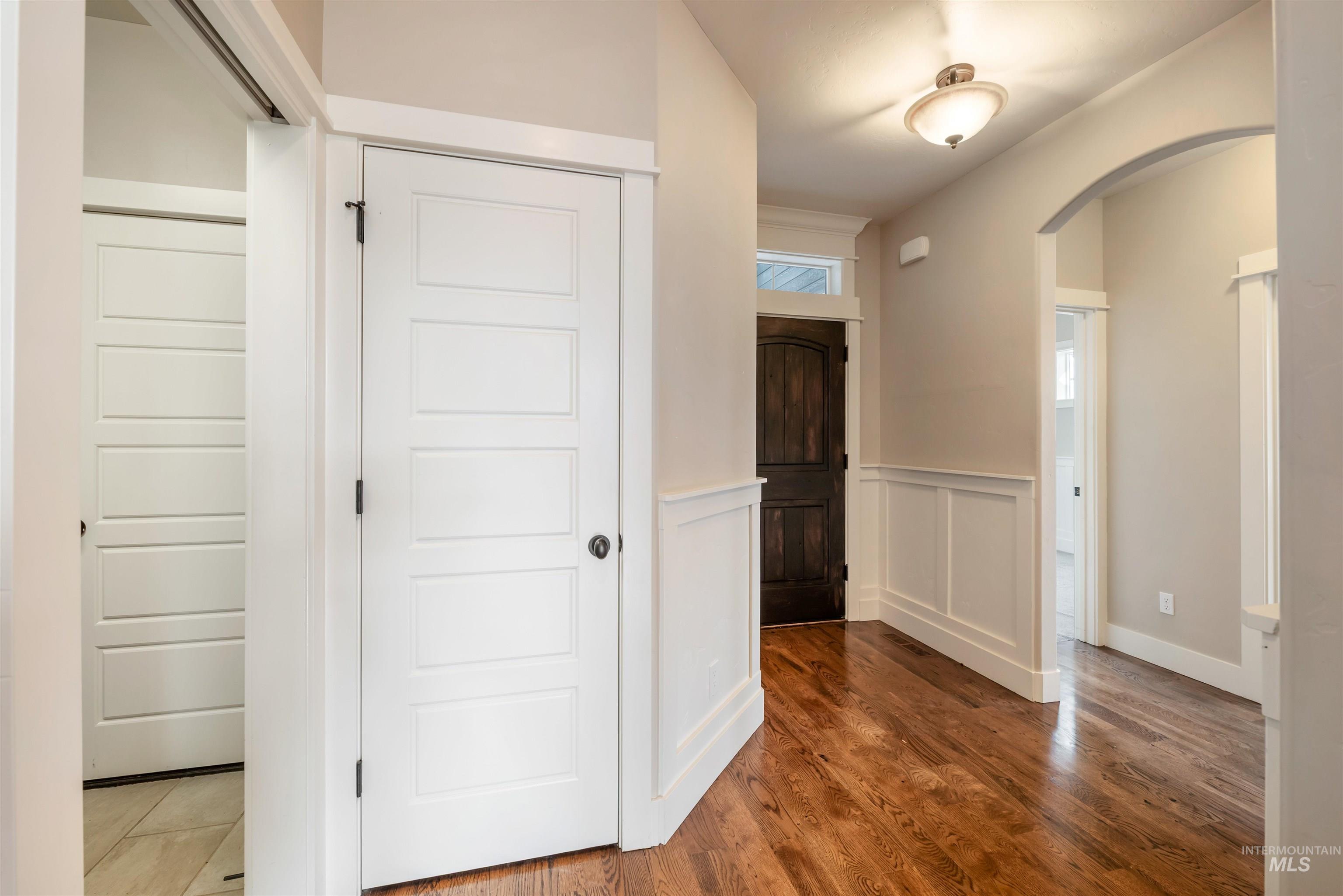 Corridor featuring wainscoting, arched walkways, a decorative wall, and wood finished floors
