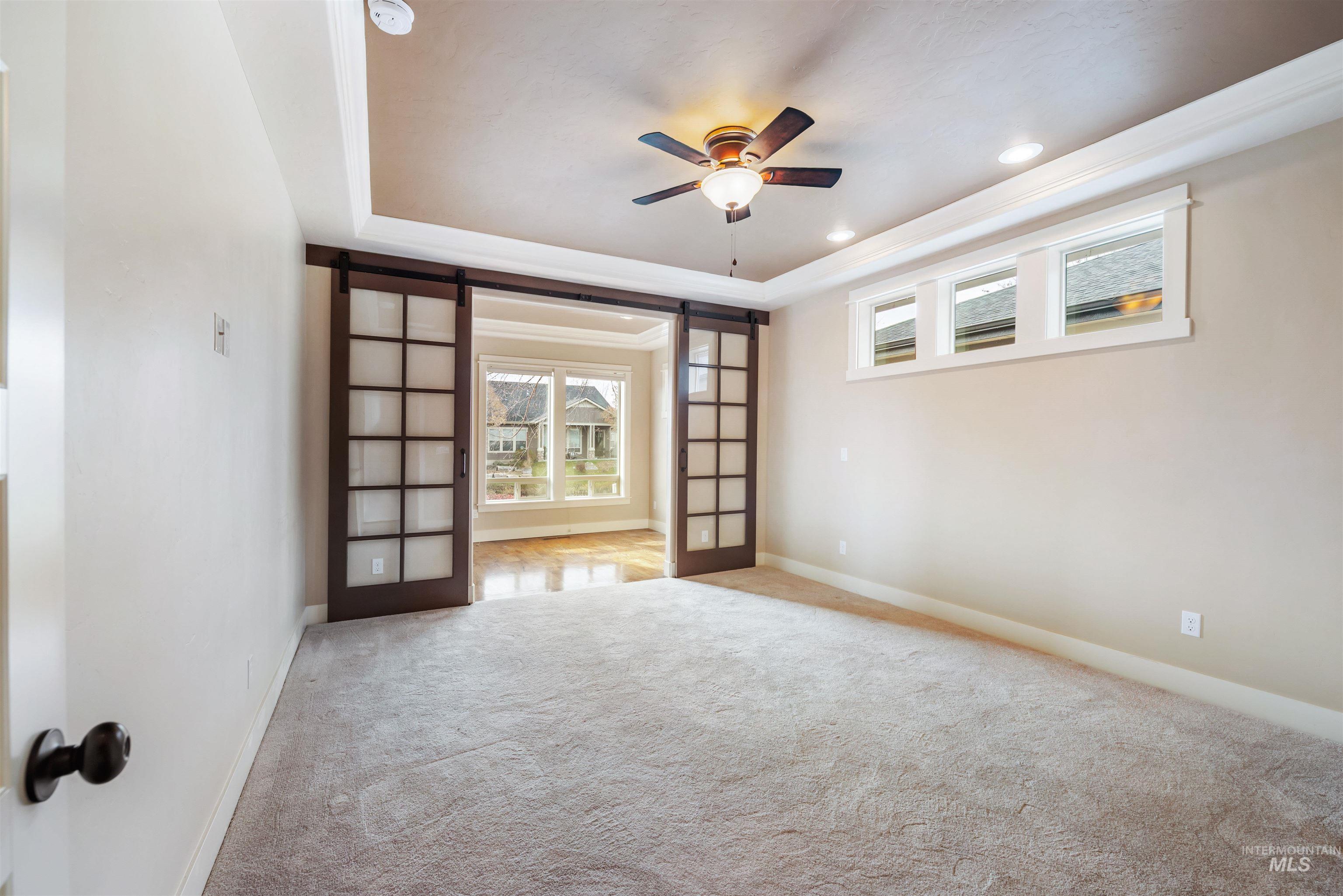 Spare room featuring a barn door, a raised ceiling, a ceiling fan, carpet flooring, and crown molding