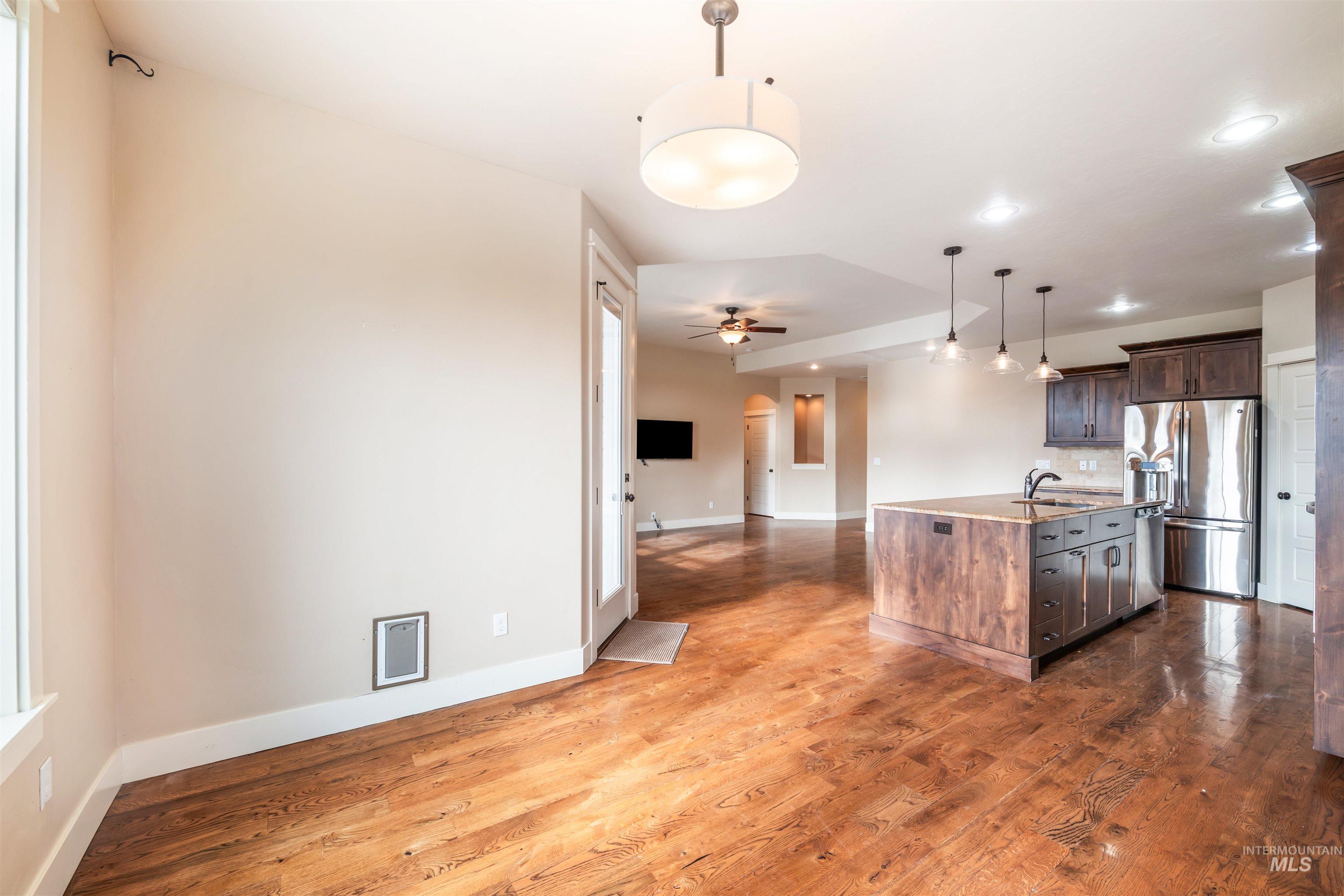 Kitchen featuring open floor plan, decorative light fixtures, appliances with stainless steel finishes, an island with sink, and dark wood finished floors
